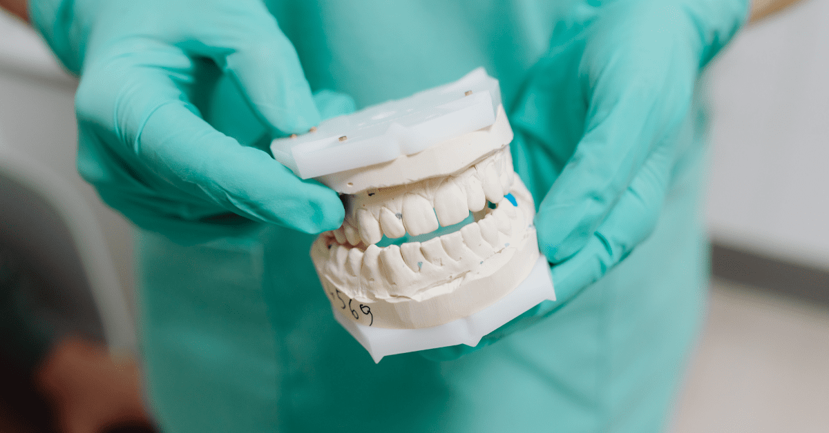 **Short alt text:** Dental model showing full-arch implant restoration held by clinician